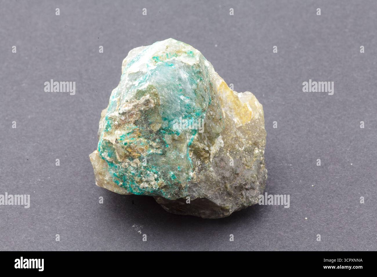 Un échantillon minéral rugueux et multicolore avec des nuances de vert, blanc et bronzé est placé au centre sur un fond gris foncé lisse. Appelé Dioptas. Banque D'Images