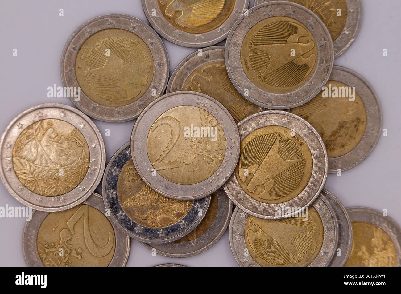Gros plan de pièces de 2 euros dispersées sur une surface gris clair, montrant divers dessins nationaux et la face européenne commune. Banque D'Images