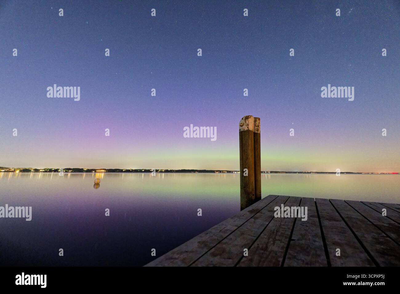 Un quai en bois calme atteint la mer tandis que des bandes lumineuses d'aurores bleu violet et jaune se répandent dans le ciel et les couleurs éclatantes reflètent gent Banque D'Images