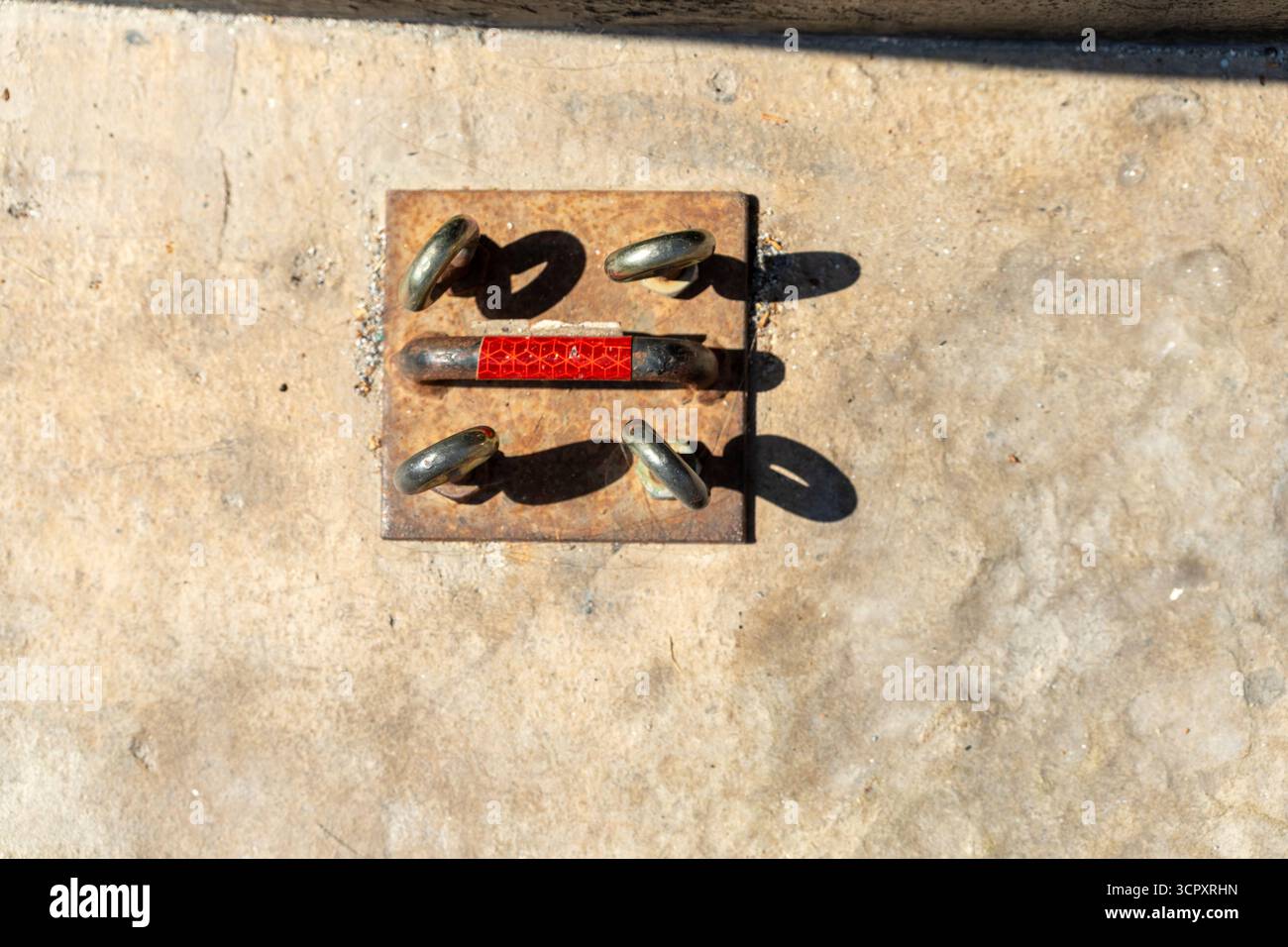 Plan suspendu de cinq anneaux et une barre avec ruban réfléchissant reposant sur une plaque carrée en métal rouillé sur une surface en béton, avec des ombres projetées. Banque D'Images Plan suspendu de cinq anneaux et une barre avec ruban réfléchissant reposant sur une plaque carrée en métal rouillé sur une surface en béton, avec des ombres projetées. Banque D'Images