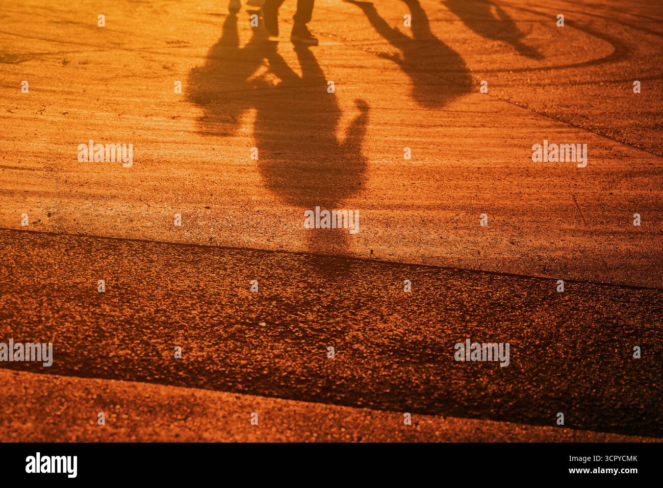 Groupe de personnes projetant de longues ombres sur la route asphaltée pendant le coucher du soleil d'été. Mise au point sélective. Banque D'Images