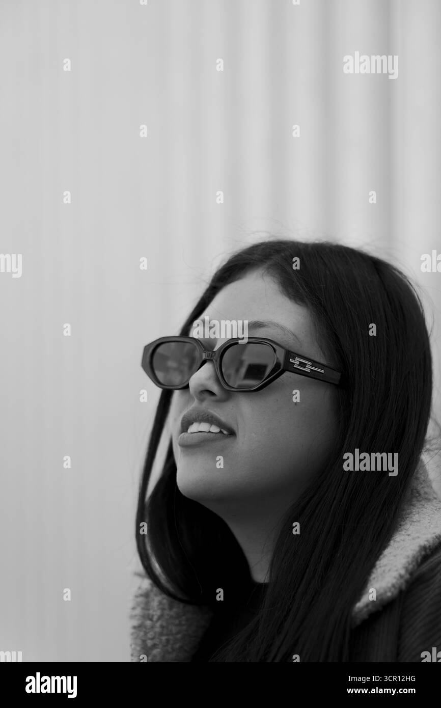 Portrait d'une jeune femme aux longs cheveux droits et à la veste grise, debout près d'un hôpital. Capturé avec lumière naturelle et faible profondeur de champ Banque D'Images
