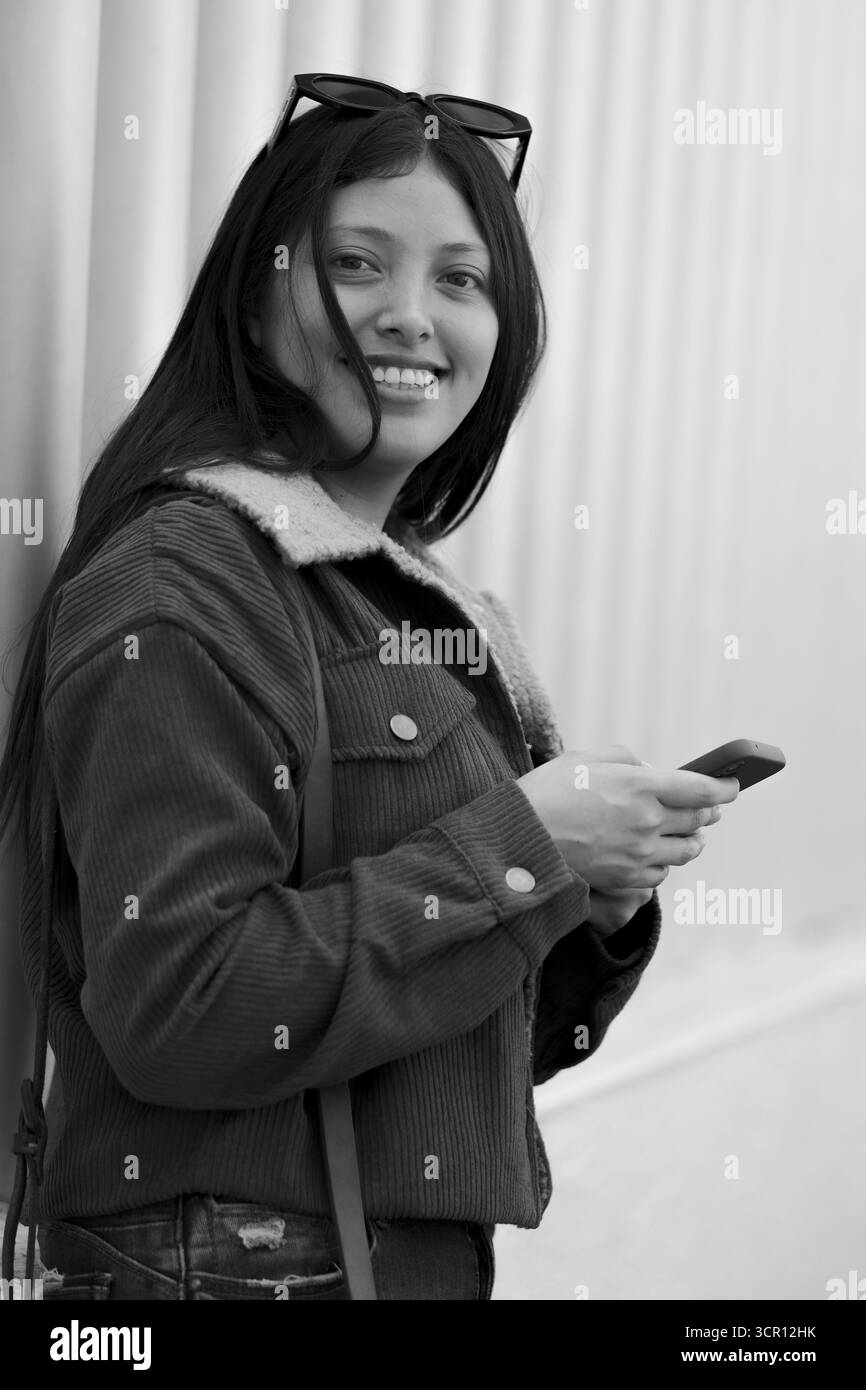 Portrait d'une jeune femme aux longs cheveux droits et à la veste grise, debout près d'un hôpital. Capturé avec lumière naturelle et faible profondeur de champ Banque D'Images