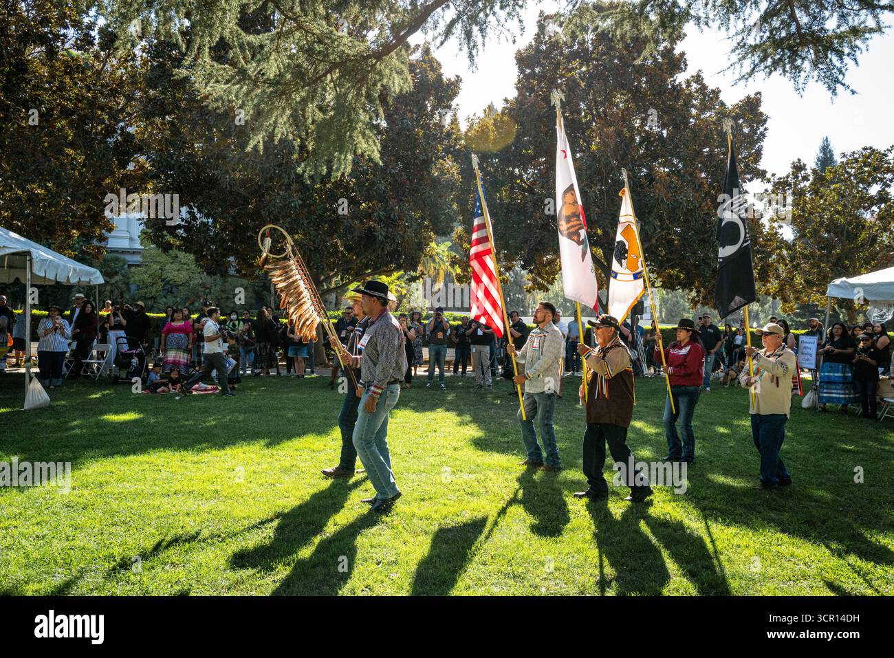 Le gardien de couleur marche avec des plumes d'aigle et des drapeaux américains, californiens et des prisonniers de guerre lors de la Journée des Indiens d'Amérique de Californie au Capitole de l'État. Banque D'Images