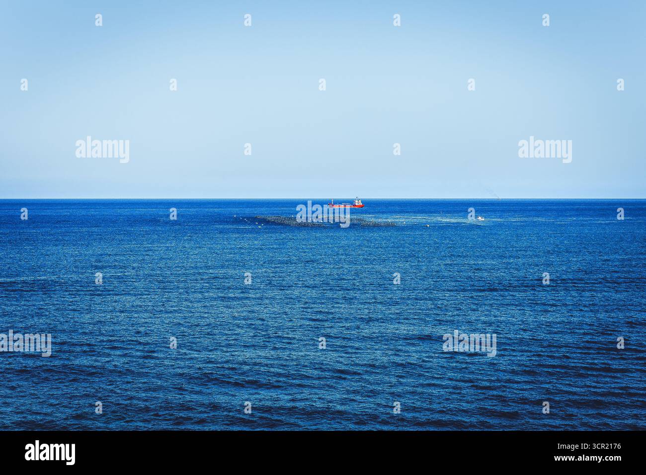 Océan bleu serein sous le ciel avec bateau de pêche rouge lointain, capturant la vie marine tranquille et l'industrie. Plan grand angle de l'immensité Banque D'Images