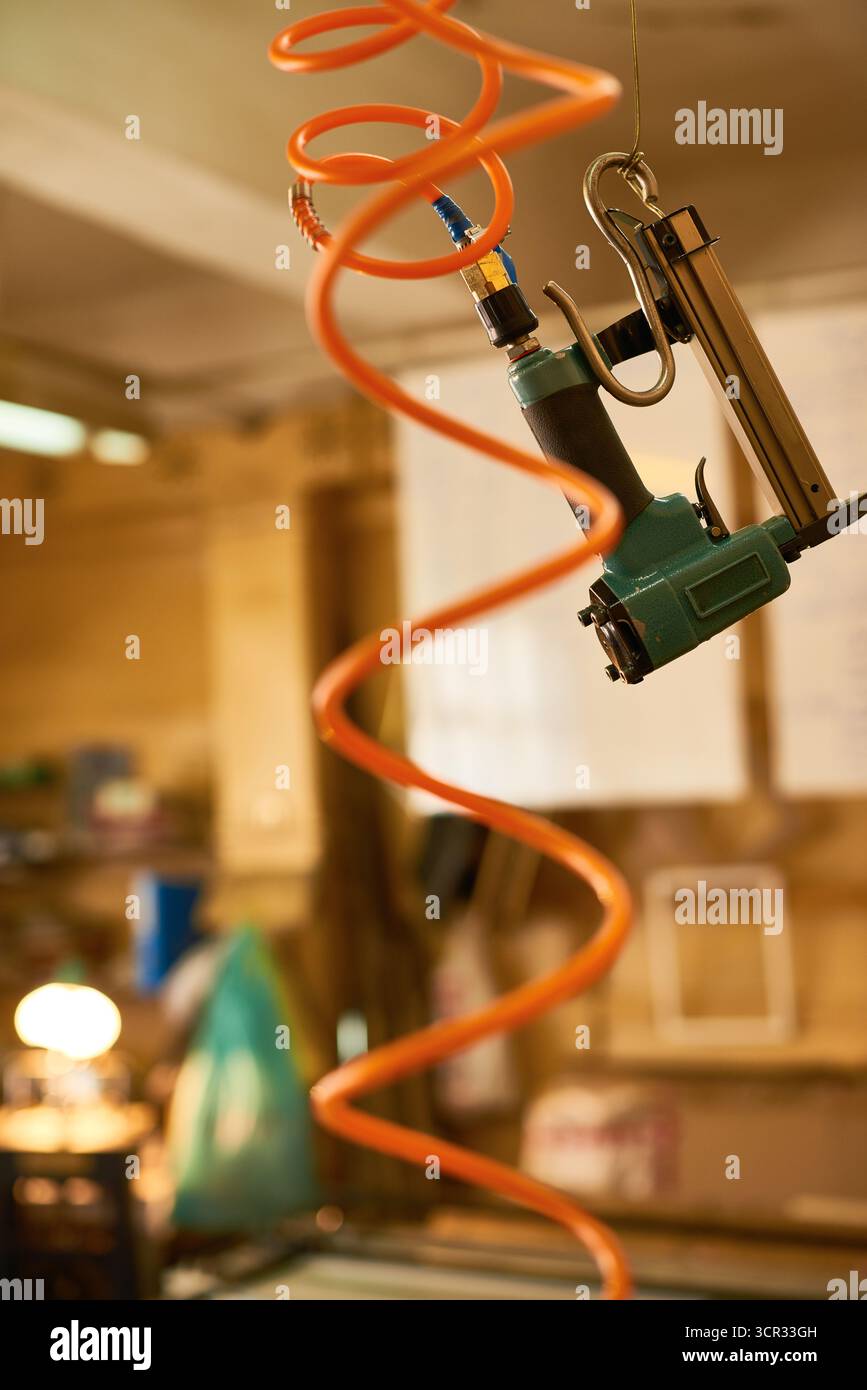 Pistolet à ongles pneumatique industriel suspendu dans un atelier avec tuyau d'air orange Banque D'Images
