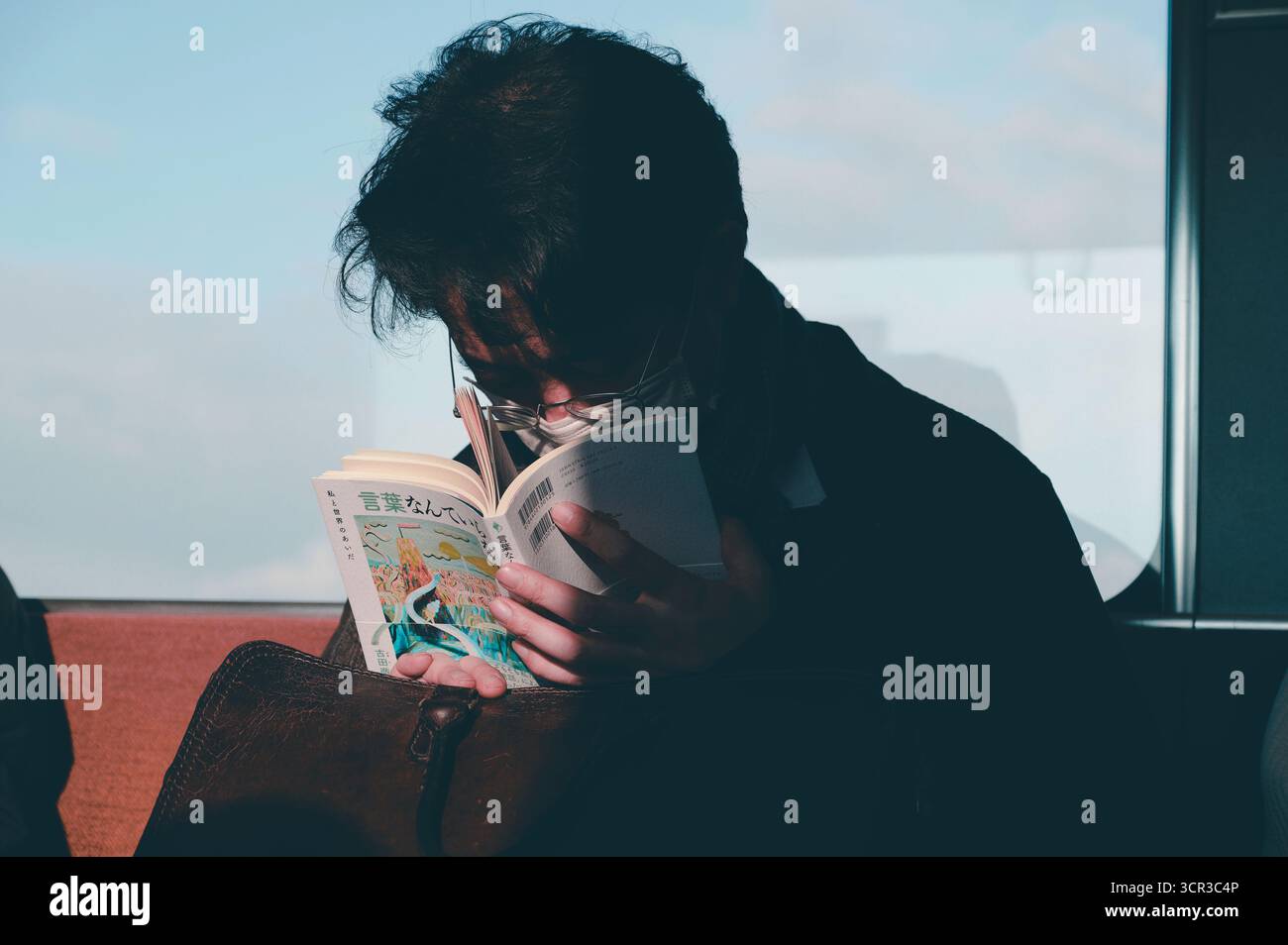 Personne portant un masque facial lit intensément sur un train, son front sillonné en profonde concentration Banque D'Images