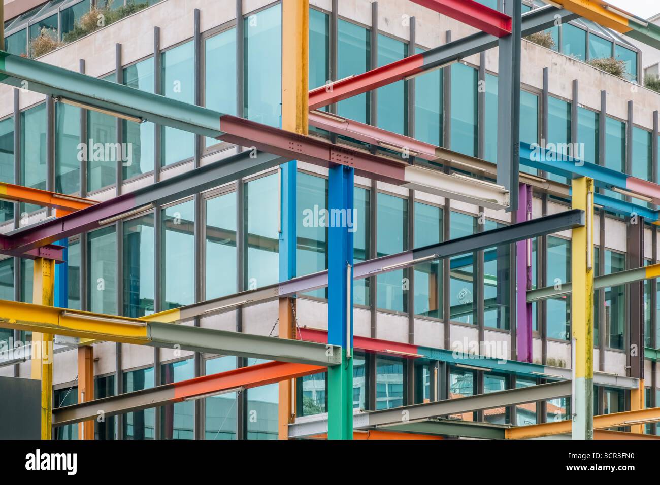 Vue abstraite d'une façade contemporaine d'immeuble de bureaux encadrée par une structure chaotique de poutres en acier peintes qui se croisent créant un motif moderne Banque D'Images