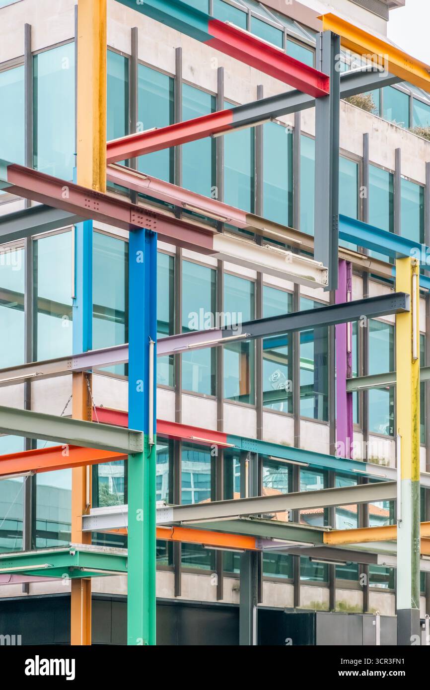 Plan abstrait vertical d'une grille colorée de poutres en acier peintes de couleurs vives qui se croisent et contrastent avec la façade vitrée d'un bâtiment contemporain Banque D'Images