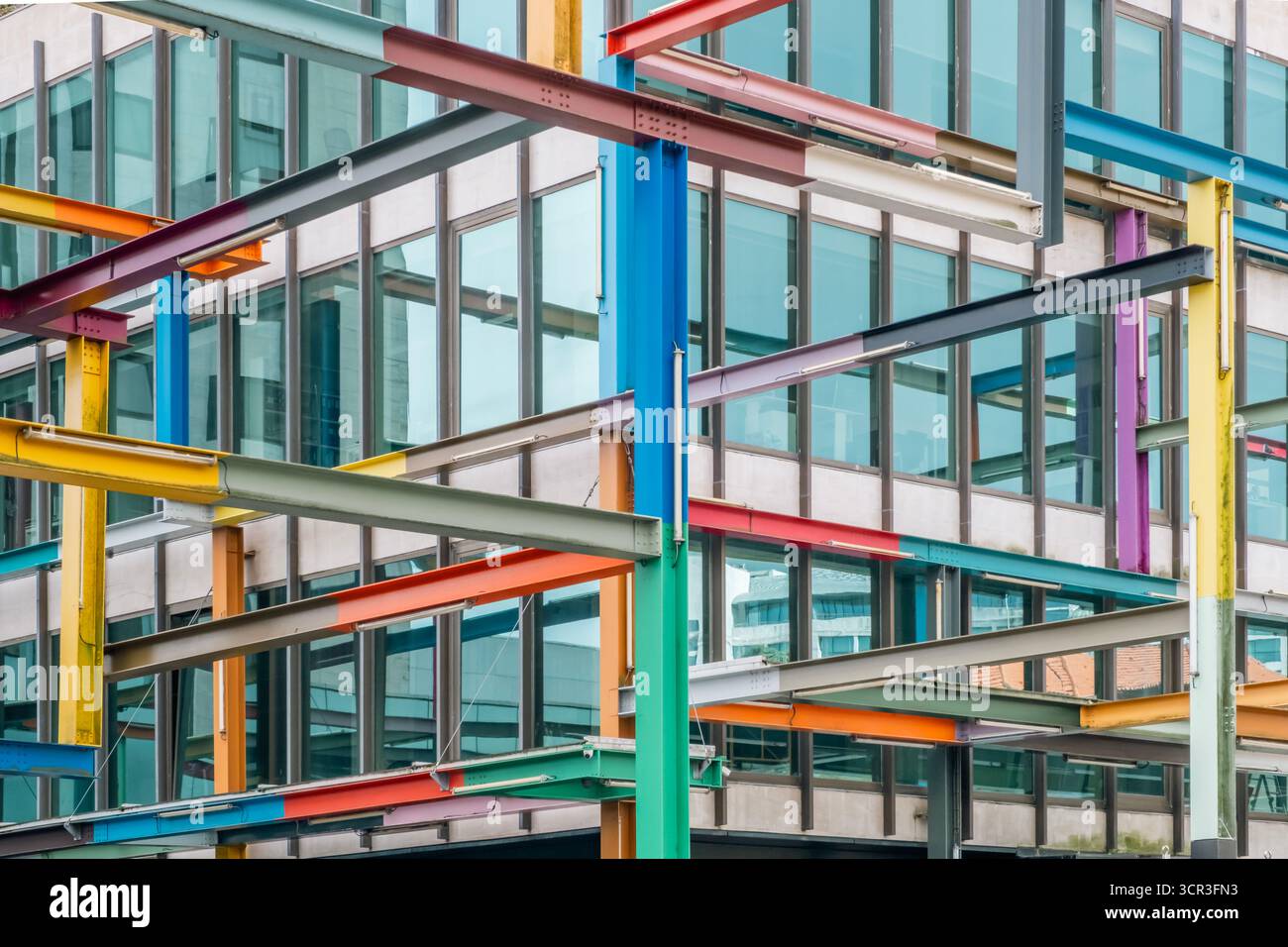 Vue abstraite plein cadre d'une installation structurelle occupée avec des poutres en acier croisées peintes de couleurs vives créant une toile complexe contre un gl moderne Banque D'Images
