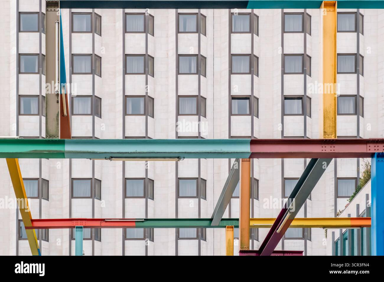 Structure métallique abstraite colorée avec des poutres et des poutres qui se croisent contre la façade répétitive en pierre texturée d'un immeuble de bureaux moderne Banque D'Images