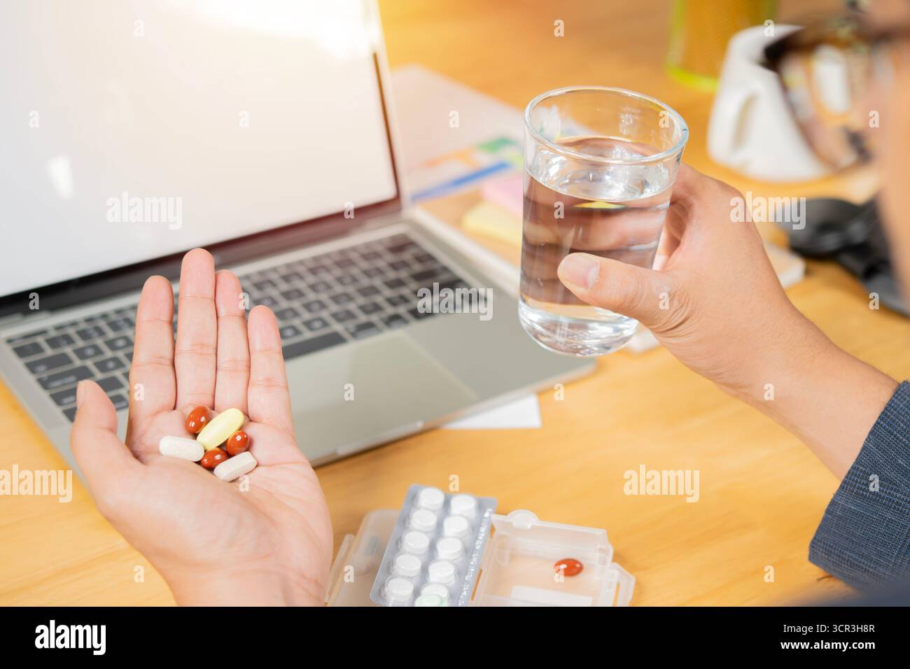 Vue arrière et foyer sélectif de l'homme d'affaires tenant de nombreux médicaments pilules et verre d'eau dans le bureau. Office syndrome concept. Banque D'Images
