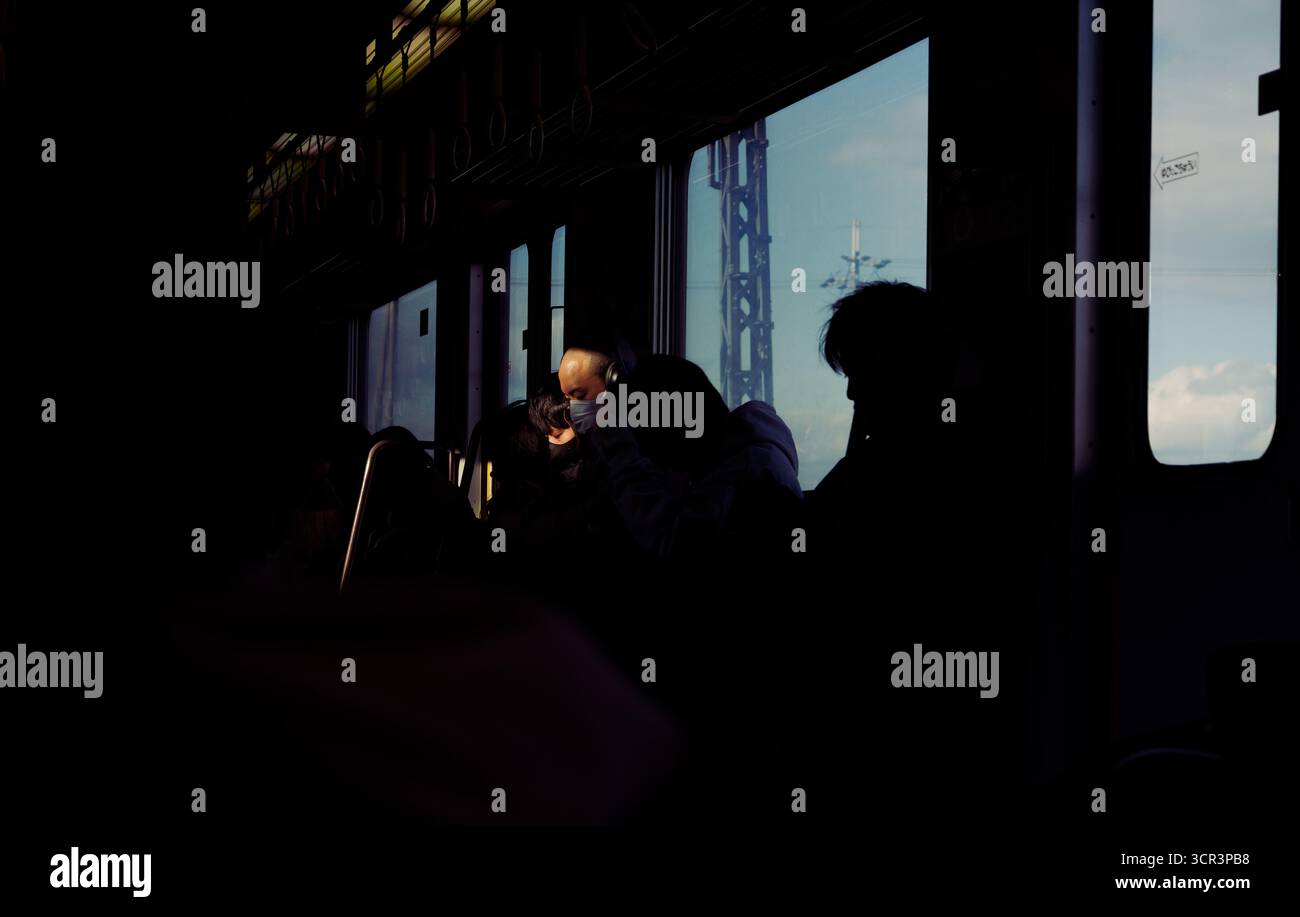 Des ombres et de la lumière douce du soleil tombent sur les passagers d'un train à Osaka, alors que le monde extérieur passe devant des lignes électriques et un ciel bleu Banque D'Images