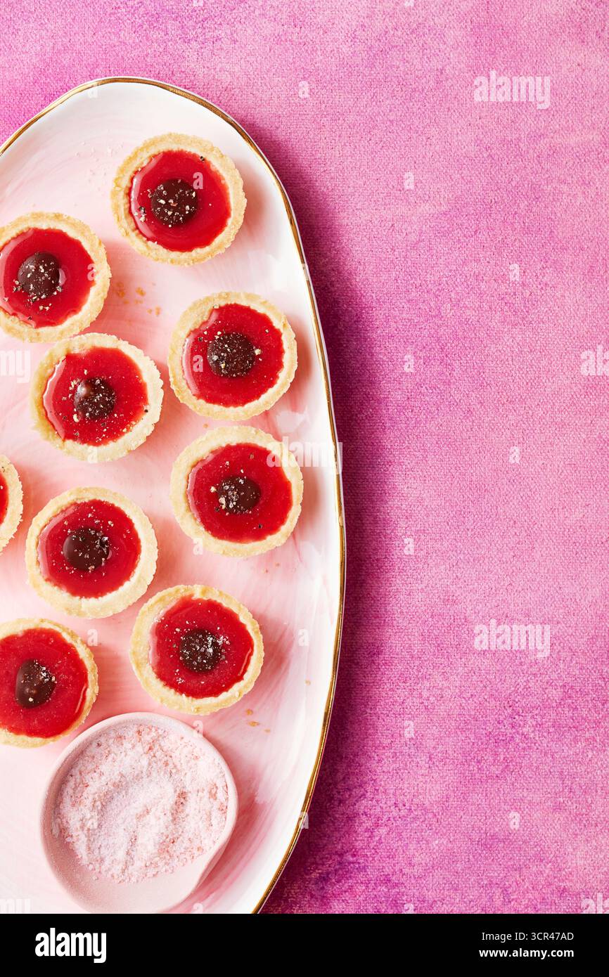 Tartes aux cerises et sucre dans un plat rose sur un fond rose texturé. Banque D'Images