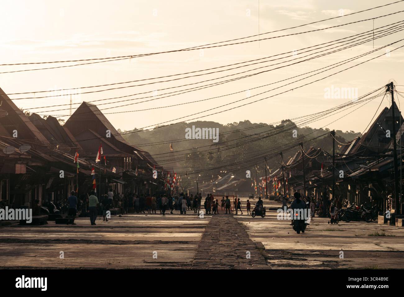 Une rue de village animée pendant le coucher du soleil avec des silhouettes et des montagnes lointaines. Desa Hilisimaetano à Nias Sud, Sumatra Nord, Indonésie Banque D'Images Une rue de village animée pendant le coucher du soleil avec des silhouettes et des montagnes lointaines. Desa Hilisimaetano à Nias Sud, Sumatra Nord, Indonésie Banque D'Images