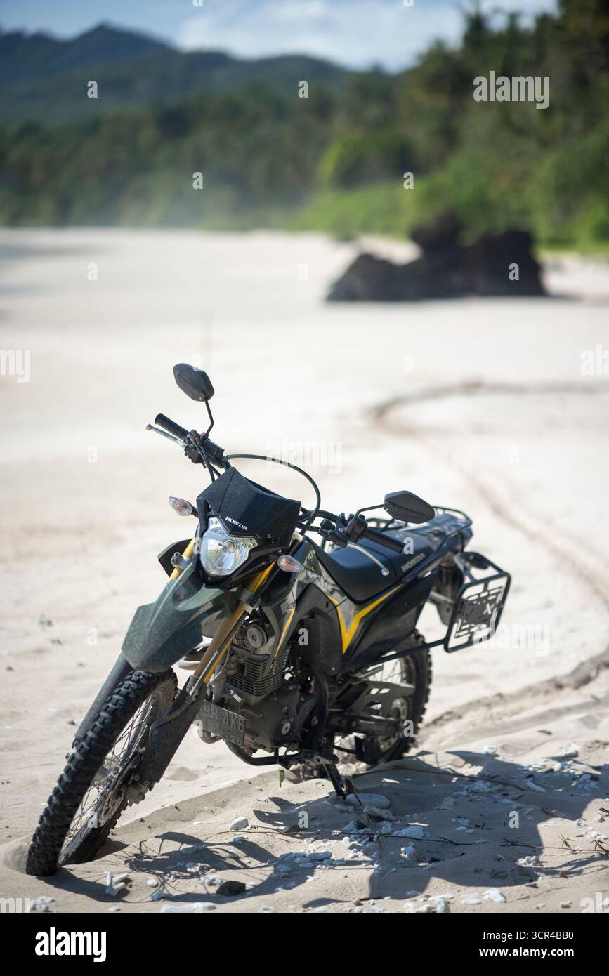 Moto hors route garée sur une plage de sable avec une végétation luxuriante en arrière-plan. Nias du Sud, Sumatra du Nord, Indonésie Banque D'Images Moto hors route garée sur une plage de sable avec une végétation luxuriante en arrière-plan. Nias du Sud, Sumatra du Nord, Indonésie Banque D'Images