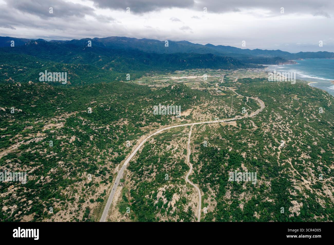Vue aérienne d'une route sinueuse à travers un paysage montagneux verdoyant et luxuriant sous un ciel nuageux. District de Ninh Hai, Ninh Thuan, Vietnam Banque D'Images