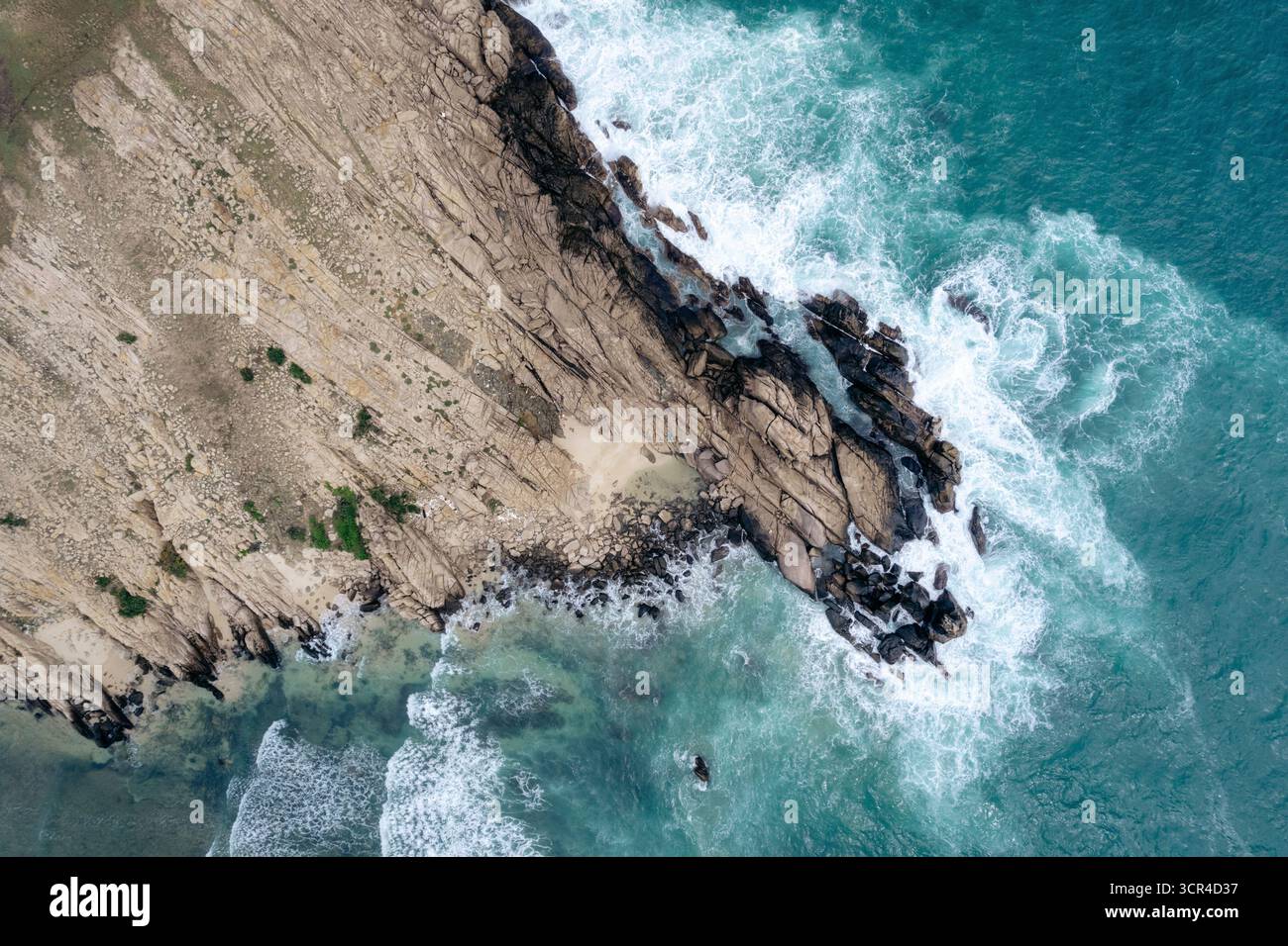 Vue aérienne de la côte accidentée avec des vagues turquoises s'écrasant contre des falaises rocheuses. District de Ninh Hai, Ninh Thuan, Vietnam Banque D'Images