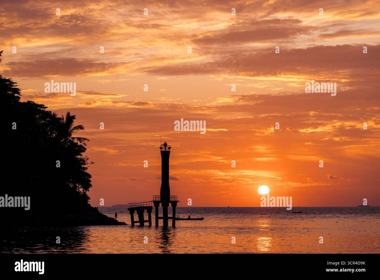 Coucher de soleil vibrant sur l'océan avec un phare silhouette et un ciel doré. Padang, Sumatra Ouest, Indonésie Banque D'Images
