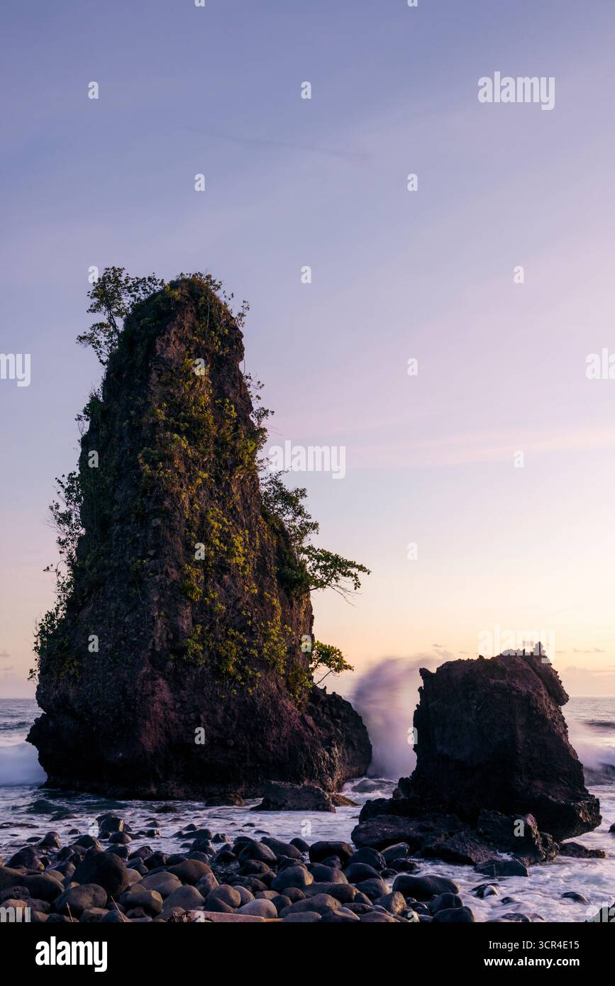 De hautes formations rocheuses au bord de l'océan pendant le coucher du soleil avec des vagues s'écrasant sur des pierres. Krui, Lampung, Sumatra, Indonésie Banque D'Images De hautes formations rocheuses au bord de l'océan pendant le coucher du soleil avec des vagues s'écrasant sur des pierres. Krui, Lampung, Sumatra, Indonésie Banque D'Images