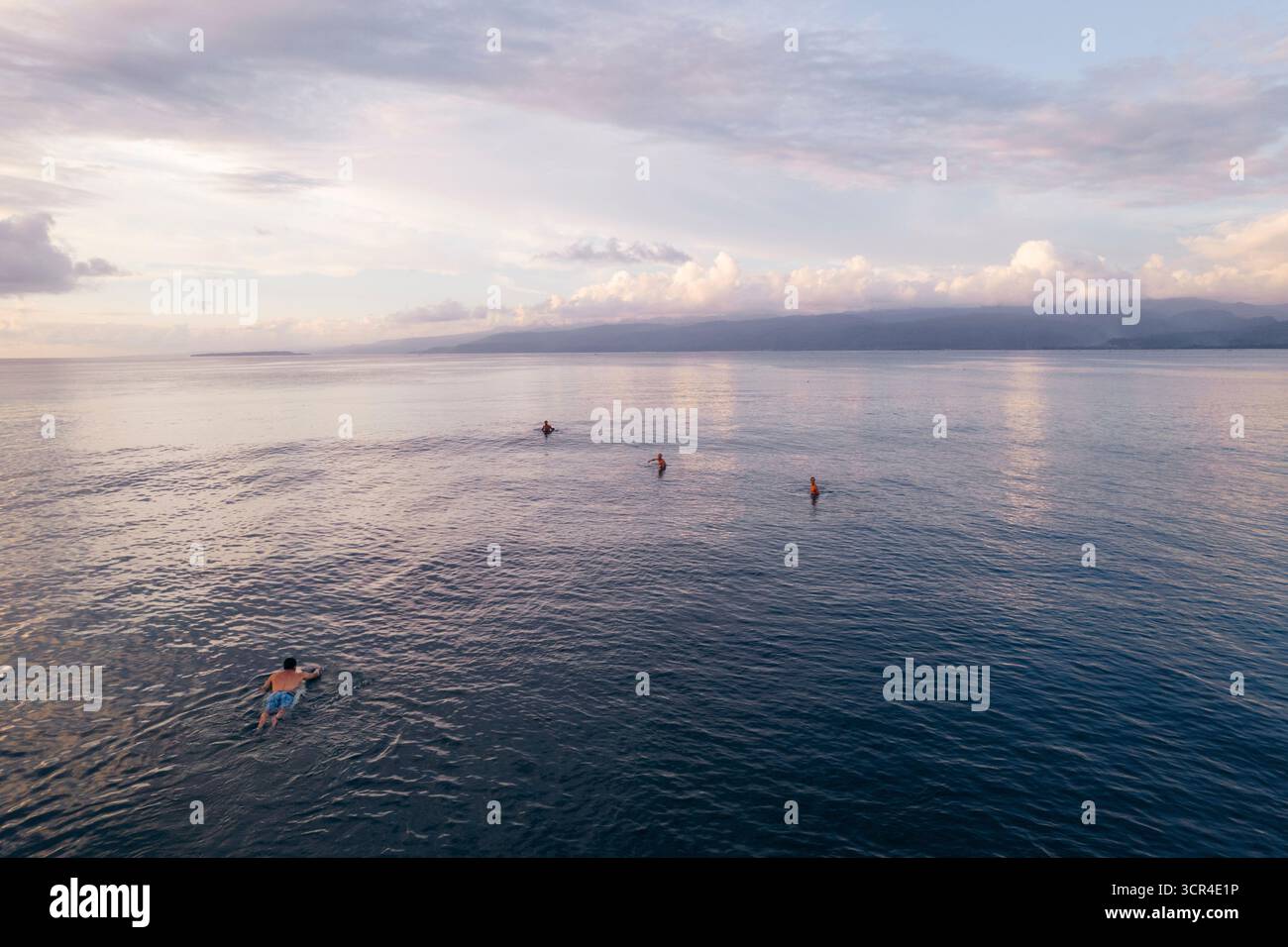 Les surfeurs pagayent sur l'océan calme au coucher du soleil avec des montagnes et des nuages lointains. Krui, Lampung, Sumatra, Indonésie Banque D'Images Les surfeurs pagayent sur l'océan calme au coucher du soleil avec des montagnes et des nuages lointains. Krui, Lampung, Sumatra, Indonésie Banque D'Images