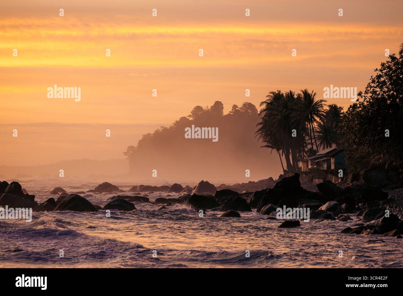 Coucher de soleil vibrant sur une plage rocheuse avec des palmiers silhouettes et une brume lointaine. Krui, Lampung, Sumatra, Indonésie Banque D'Images Coucher de soleil vibrant sur une plage rocheuse avec des palmiers silhouettes et une brume lointaine. Krui, Lampung, Sumatra, Indonésie Banque D'Images