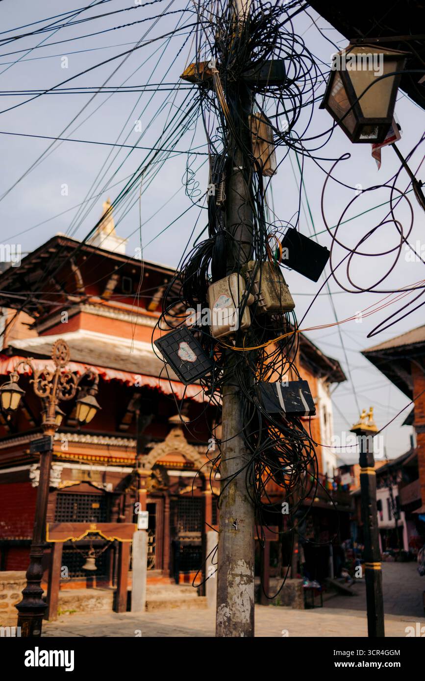 Un poteau utilitaire emmêlé avec des câbles dans une zone urbaine devant un bâtiment traditionnel. Bandipur, Népal Banque D'Images