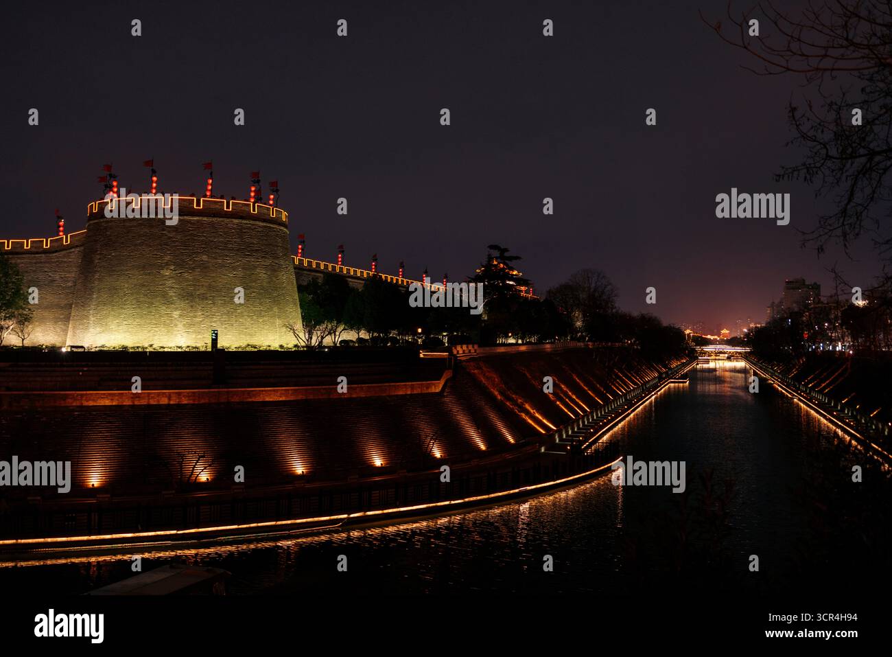 Muraille antique illuminée la nuit avec canal et arbres, un paysage urbain serein en soirée. XI'an, Chine Banque D'Images