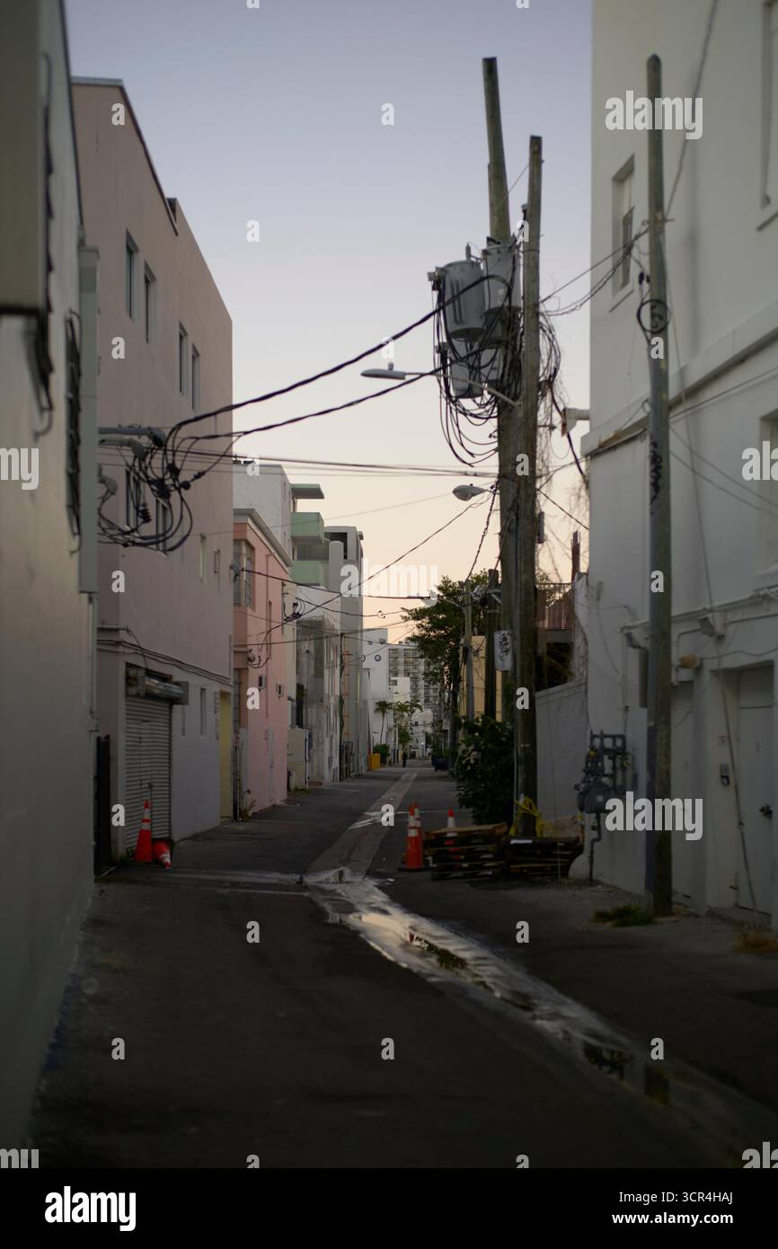 Ruelle urbaine étroite bordée de bâtiments et de poteaux électriques au coucher du soleil. Miami, Floride, États-Unis Banque D'Images