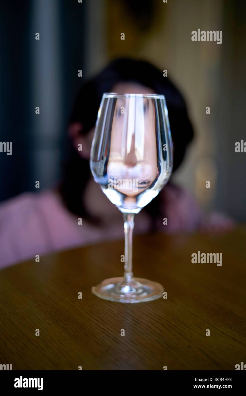 Verre d'eau avec un reflet de visage déformé sur une table en bois. Banque D'Images