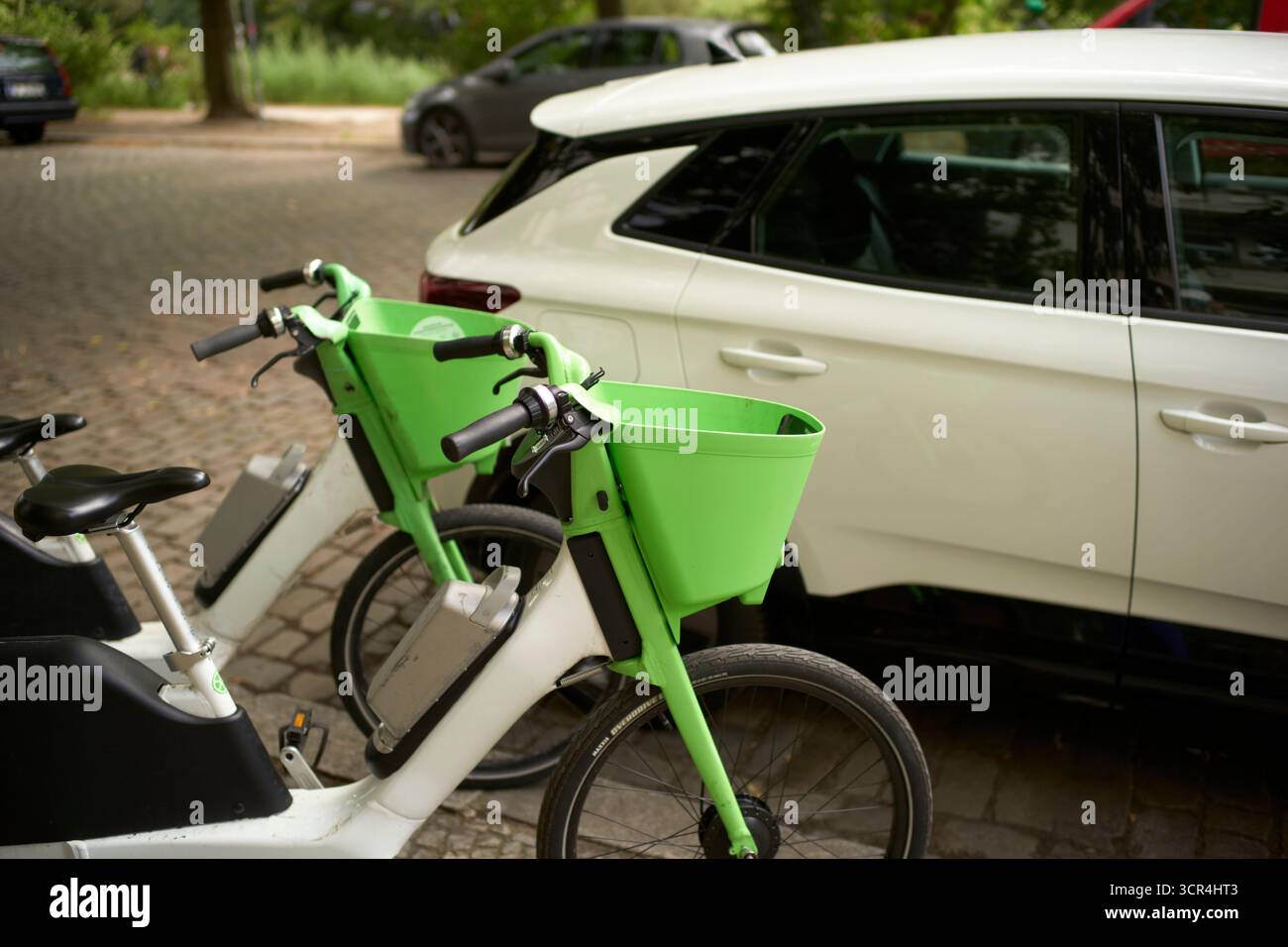 Vélos électriques verts garés à côté d'une voiture blanche dans une rue pavée. Berlin, Allemagne Banque D'Images
