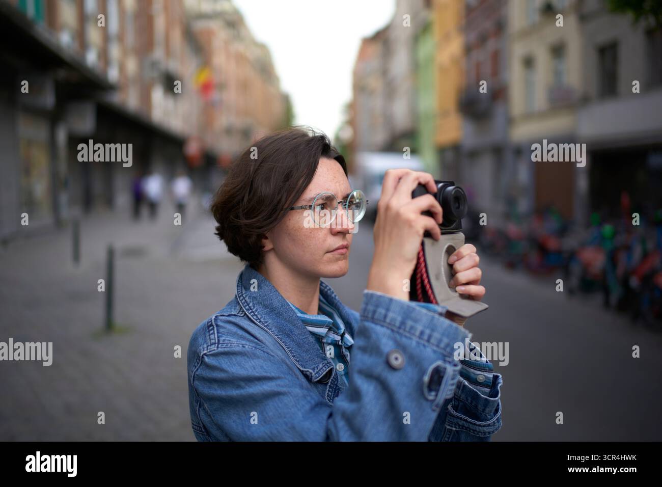 Jeune femme en veste denim photographiant la rue de la ville avec un fond flou. Bruxelles, Belgique Banque D'Images