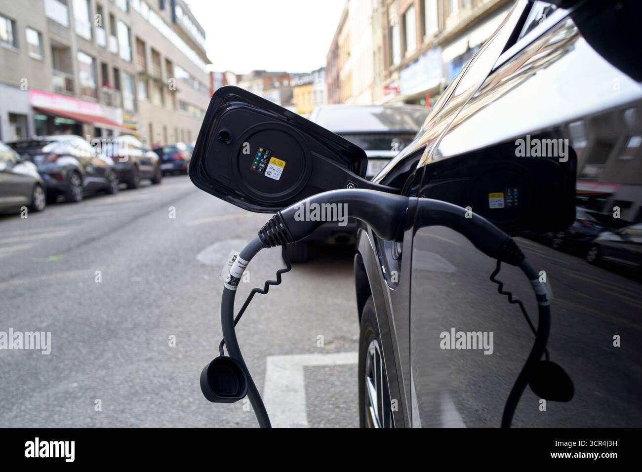 Voiture électrique branchée sur une borne de recharge dans une rue de la ville, entourée de bâtiments et de voitures garées. Allemagne Banque D'Images