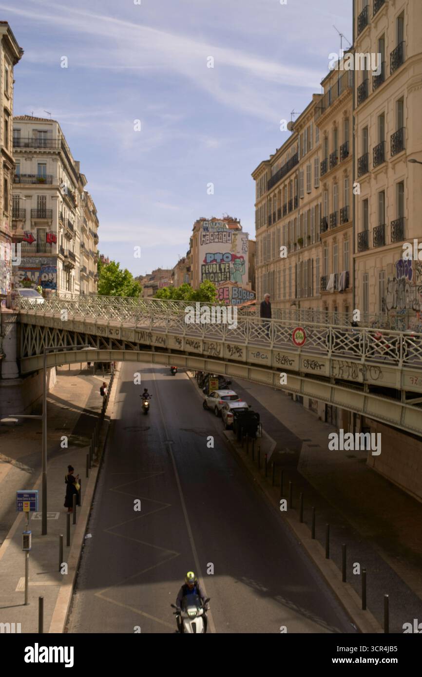 Scène urbaine avec des motocyclistes sous des bâtiments couverts de graffitis et un pont piétonnier. Marseille, France Banque D'Images