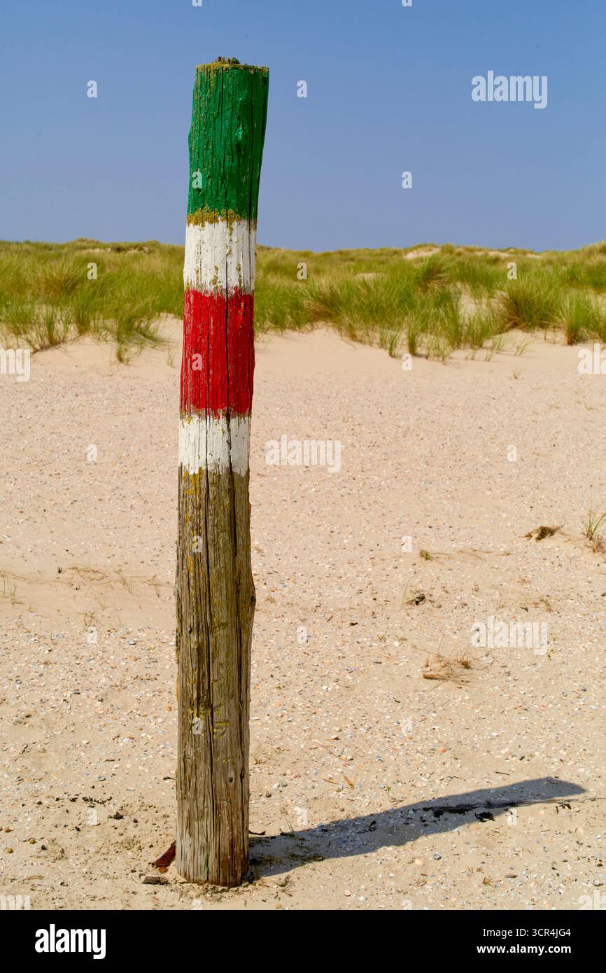 Poteau en bois peint avec des rayures vertes, blanches et rouges sur une plage de sable avec de l'herbe. Mer du Nord, Allemagne Banque D'Images