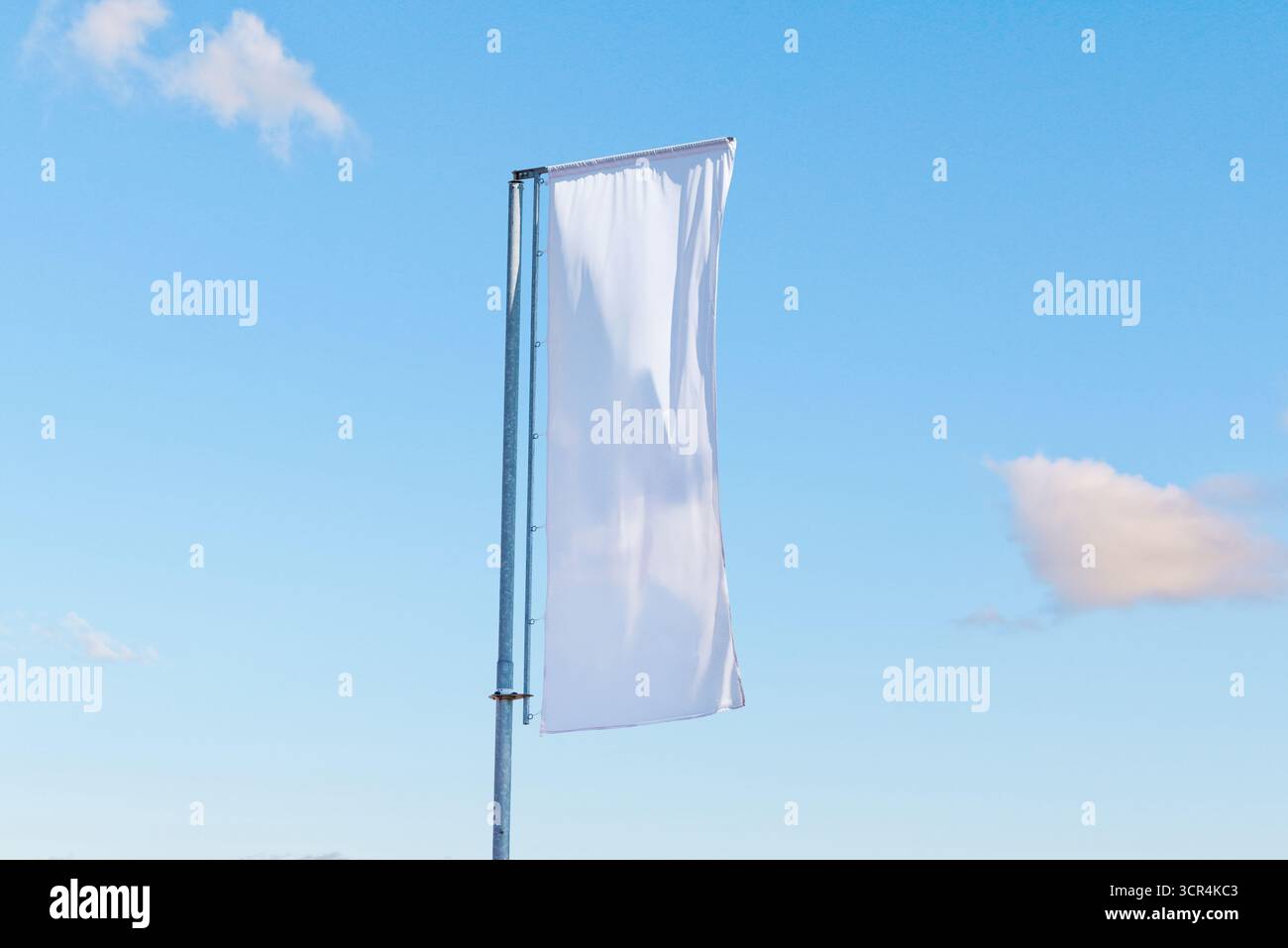 Drapeau publicitaire blanc vertical sur le poteau métallique flottant dans le vent sous le ciel bleu clair, modèle promotionnel minimal Banque D'Images