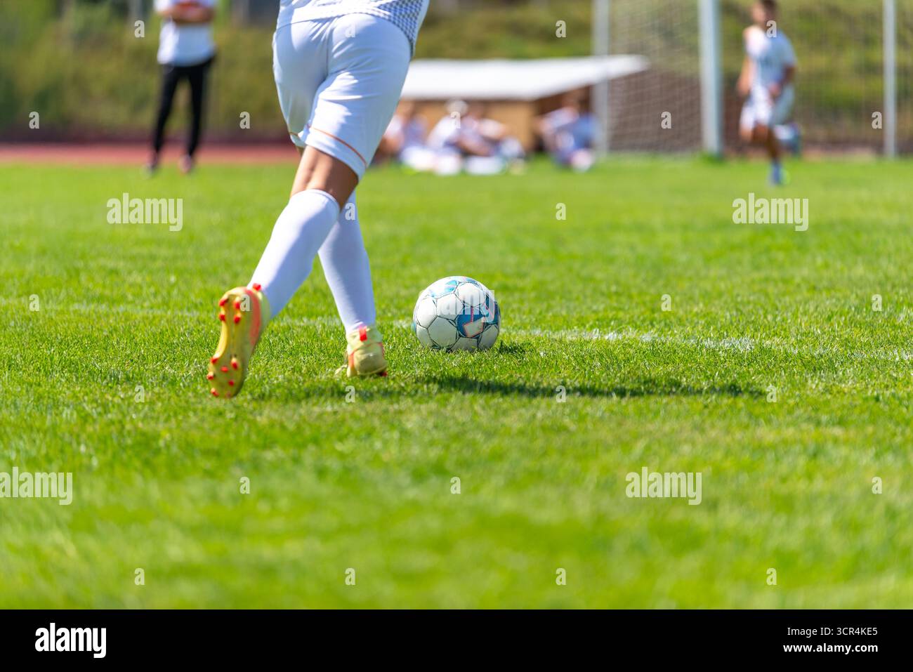 Gros plan d'un jeune joueur de football en uniforme blanc donnant des coups de pied sur le terrain. Banque D'Images