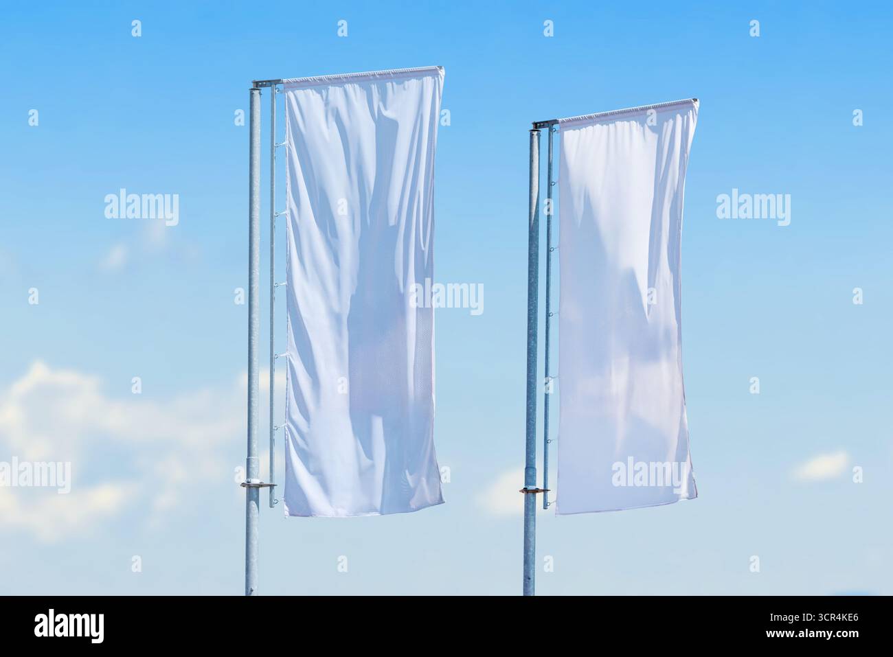 Deux grands drapeaux blancs verticaux ondulant sur des poteaux métalliques contre le ciel bleu clair, concept minimaliste de publicité extérieure Banque D'Images