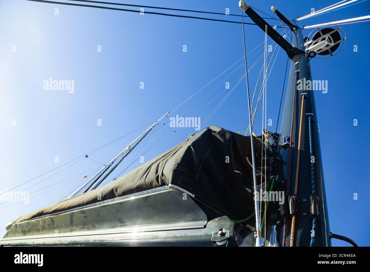 Le mât d'un yacht à voile avec un radar, des cordes à voile et une voile pliée, vu d'en bas contre le ciel. Banque D'Images