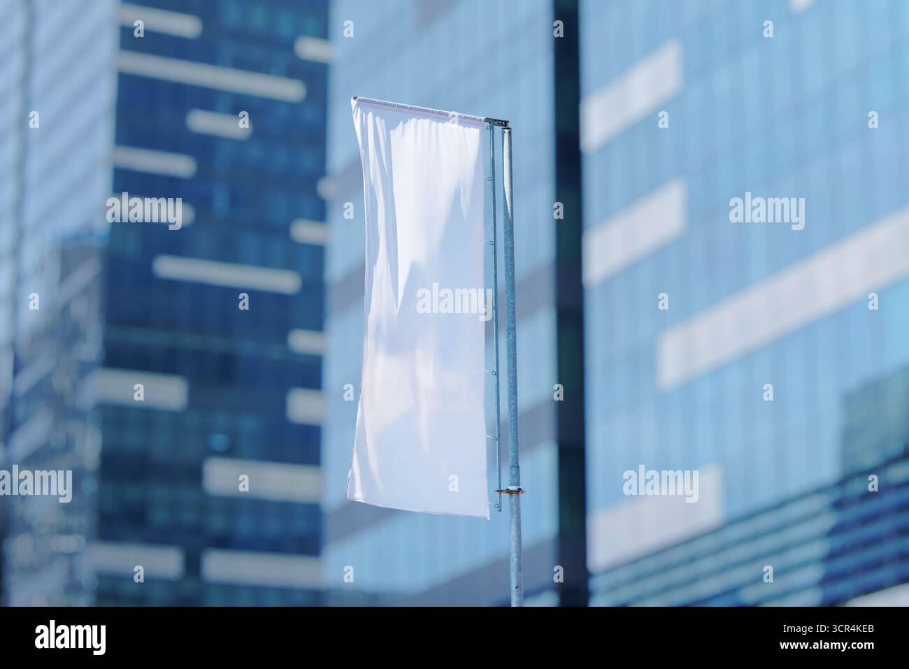 Drapeau publicitaire vertical blanc ondulant sur le poteau devant le bâtiment en verre moderne, l'image de marque extérieure et le concept de promotion des affaires. Banque D'Images