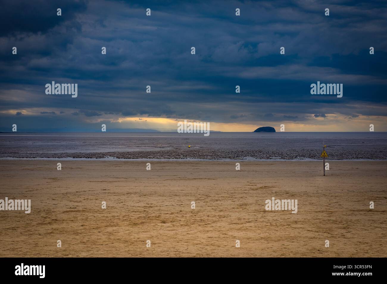 Ciel spectaculaire au-dessus d'une vaste plage. Un panneau d'avertissement avertit les spectateurs des sables mouvants. Banque D'Images
