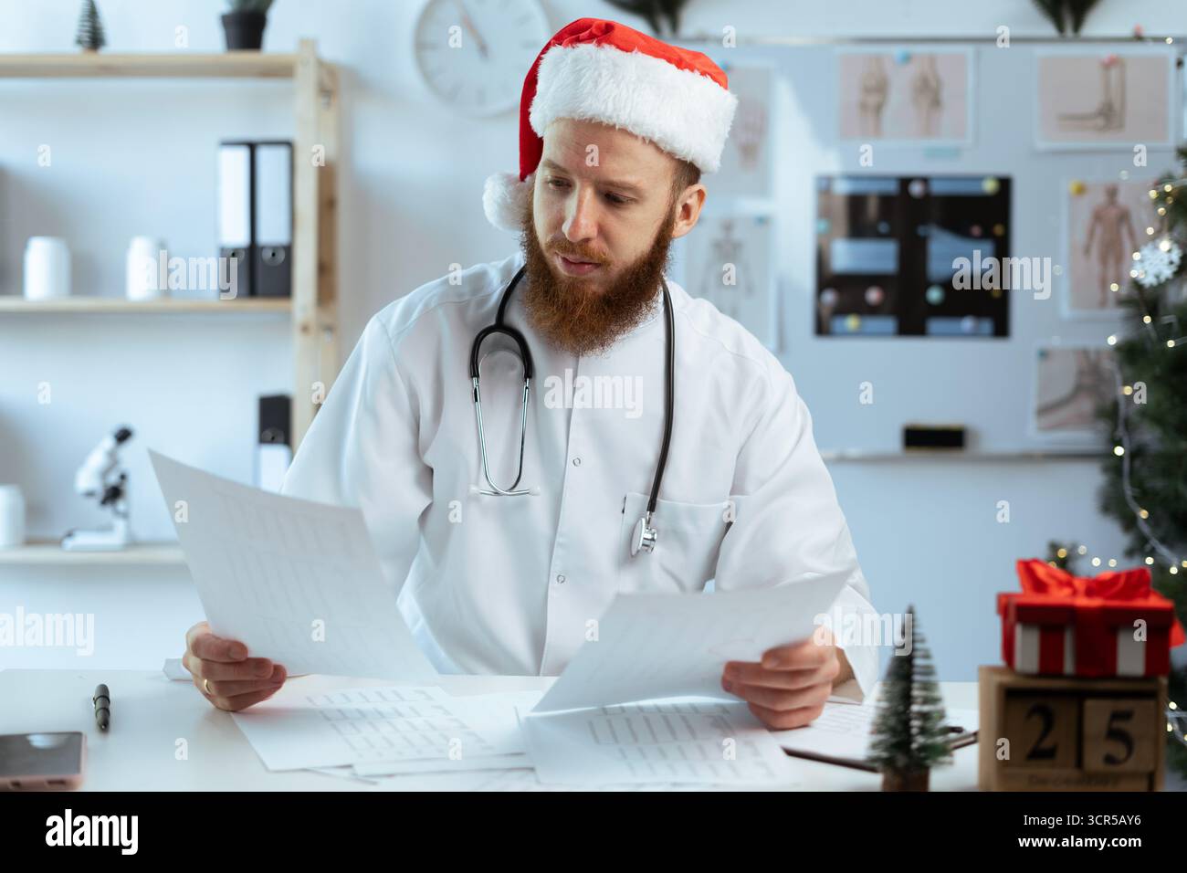 Docteur en quart de travail avec des documents papier dans le bureau de l'hôpital à la veille de noël. copier l'espace Banque D'Images