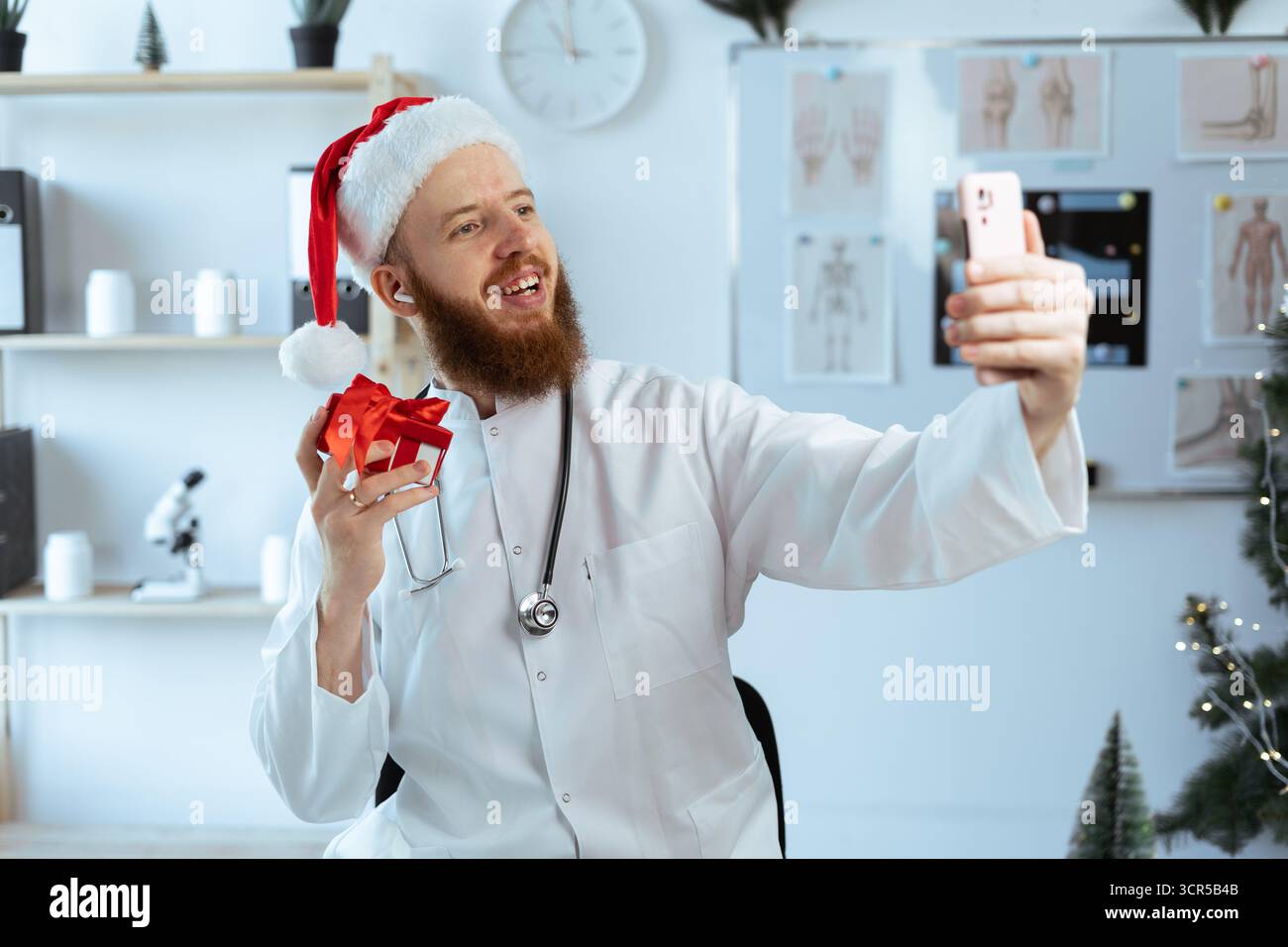 Médecin tenant une boîte-cadeau faisant selfie au smartphone sur le quart de travail à l'hôpital la veille de noël. copier l'espace Banque D'Images