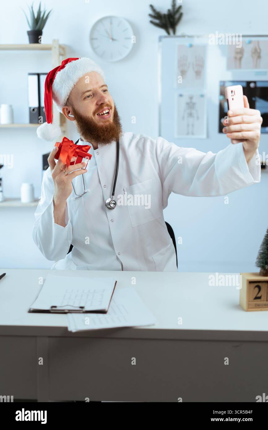 Docteur prenant photo selfie avec boîte-cadeau sur le quart de travail à l'hôpital la veille de noël. copier l'espace Banque D'Images