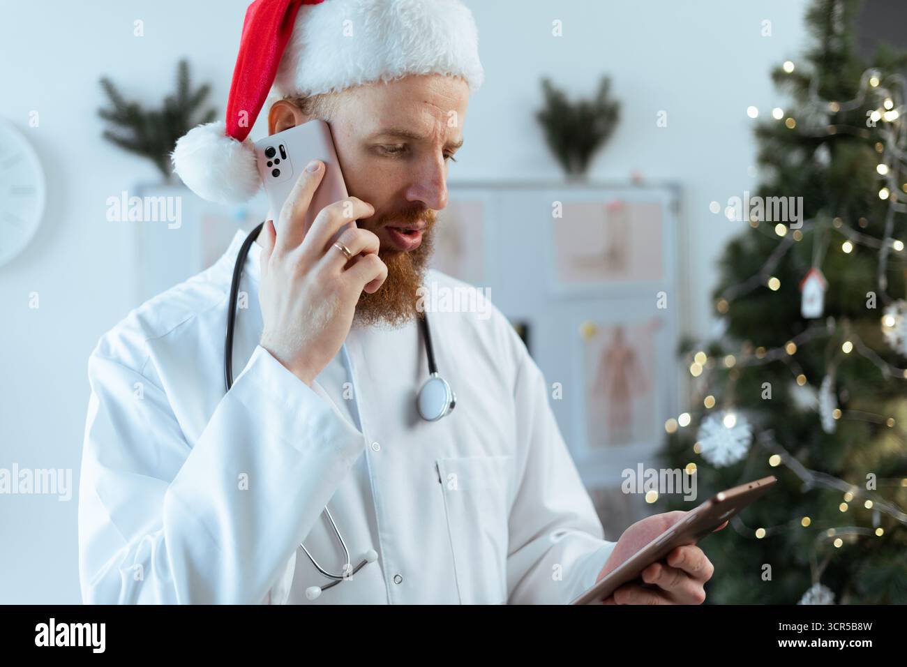 Portrait d'un médecin barbu dans un chapeau de Père Noël à l'aide d'une tablette numérique et appelant un patient en service la veille de Noël. copier l'espace Banque D'Images