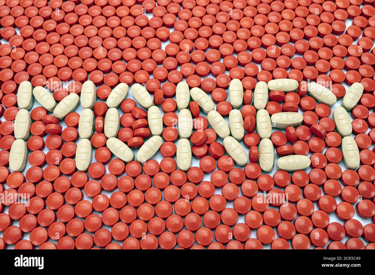 Une pilule blanche orthographiant l'argent sur fond de pilules rouges, créant un contraste frappant. l'arrangement est créatif et visuellement attrayant Banque D'Images