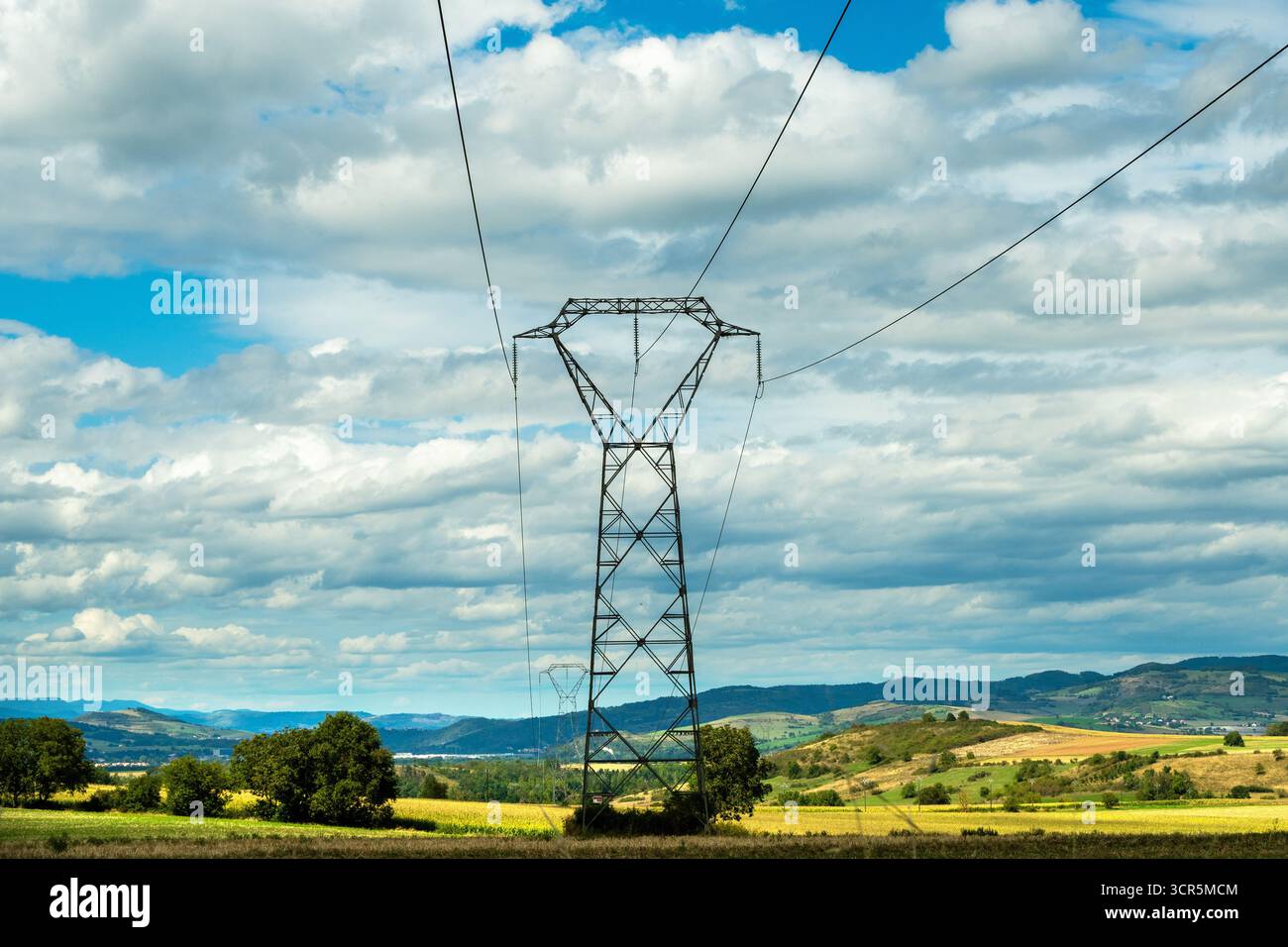 Lignes électriques à haute tension contre un ciel bleu lumineux avec des nuages éparpillés , Puy de Dôme, Auvergne Rhône Alpes, France Banque D'Images
