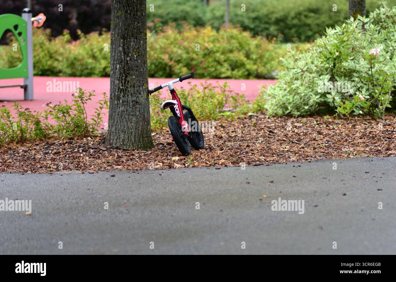 Petit vélo d'équilibre rouge appuyé contre un arbre dans le parc de jeux. Concept d'enfance, de jeu en plein air, et les enfants apprenant à monter. Banque D'Images
