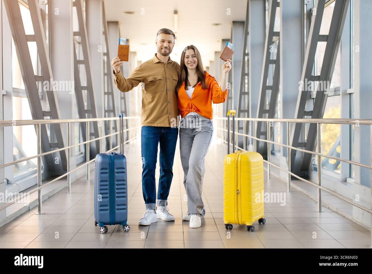 Couple heureux à l'aéroport tenant passeports et valises, prêt pour le voyage Banque D'Images