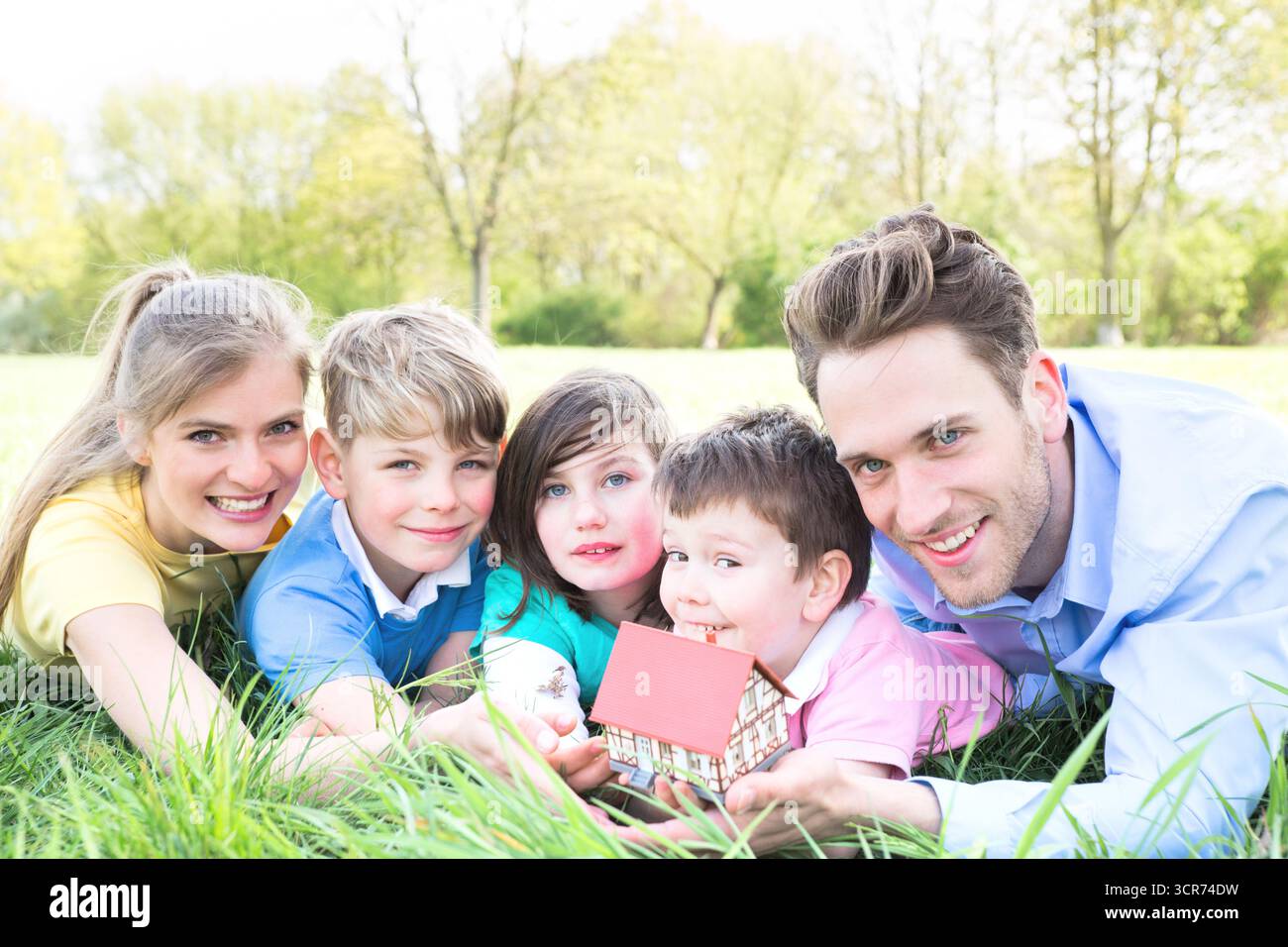 Famille avec trois enfants sur une prairie planifiant une maison individuelle Banque D'Images